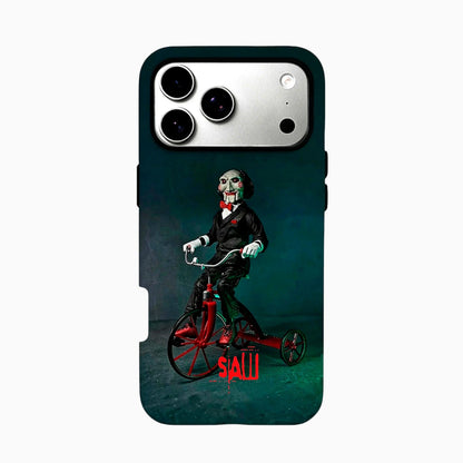 Carcasa SAW para iPhone con Billy el títere montado en su triciclo rojo sobre un fondo oscuro verde azulado.